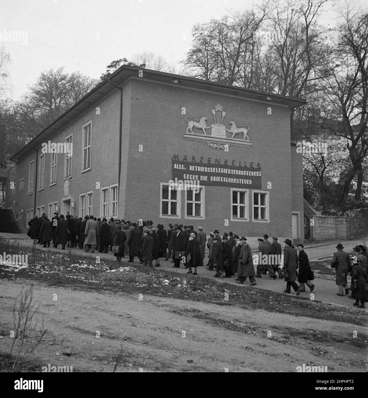 Das ehemalige Gasthaus Marchenkeller in Linz. Die Personen im Vordergrund sind Delegierte einer Betriebsdelegiertenkonferenz der KPÖ. Die Inschrift auf dem Banner lautet: Generalkonferenz der Betriebsdelegierten gegen die Kriegslohnsteuer ca. Dezember 1952 Stockfoto