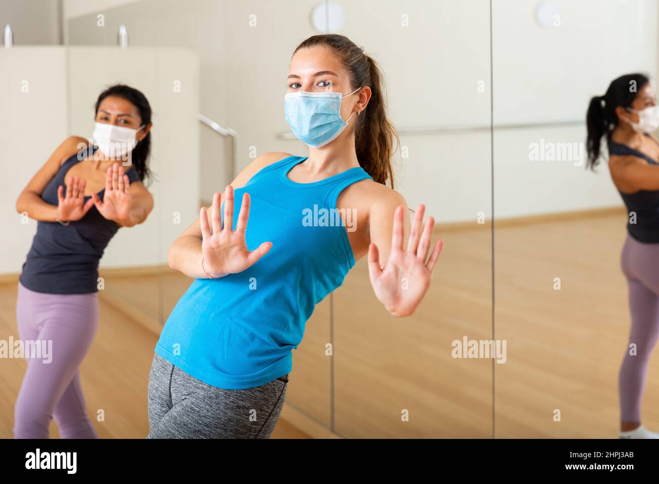 Positive Mädchen in Schutzmaske üben energischen Tanz in der Gruppe Klasse Stockfoto