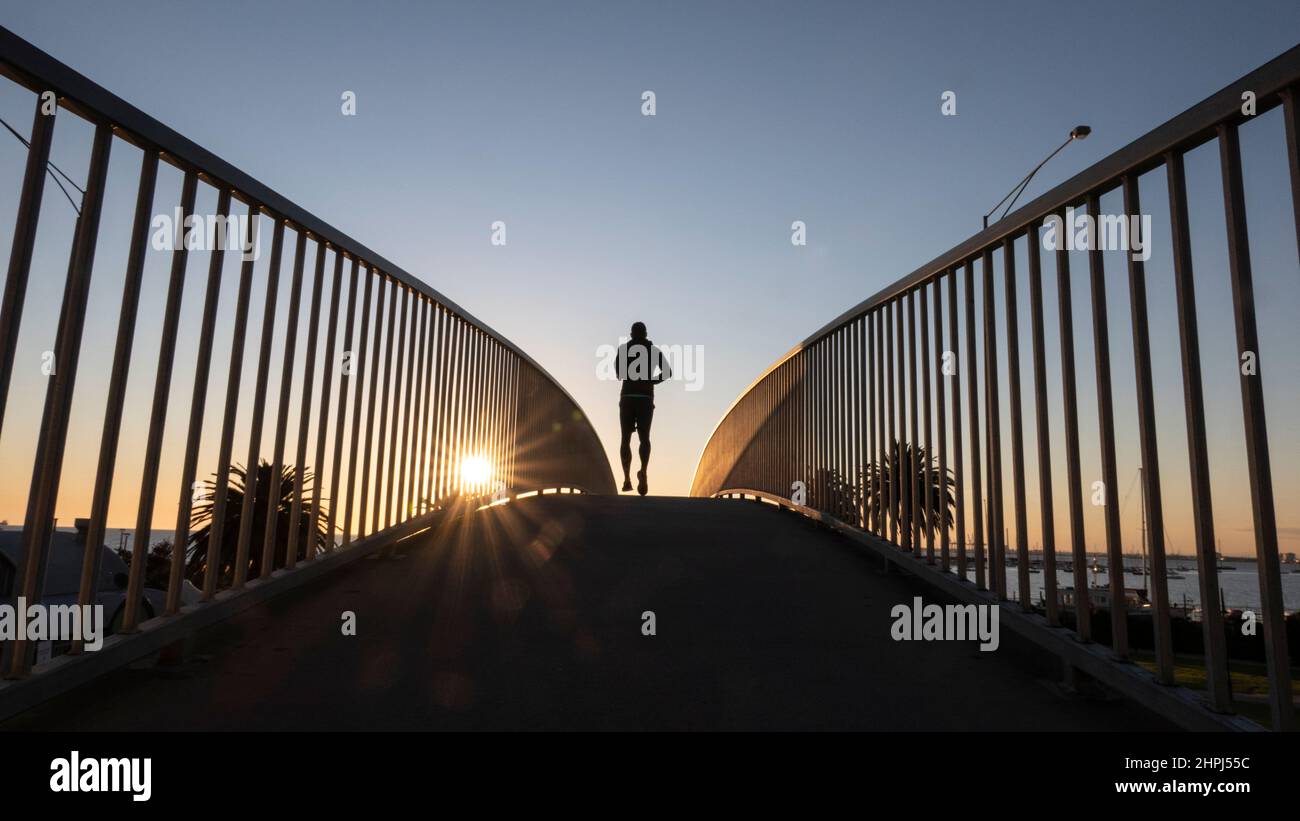Silhouette eines Einzelläufers, als er über eine Brücke geht. Stockfoto