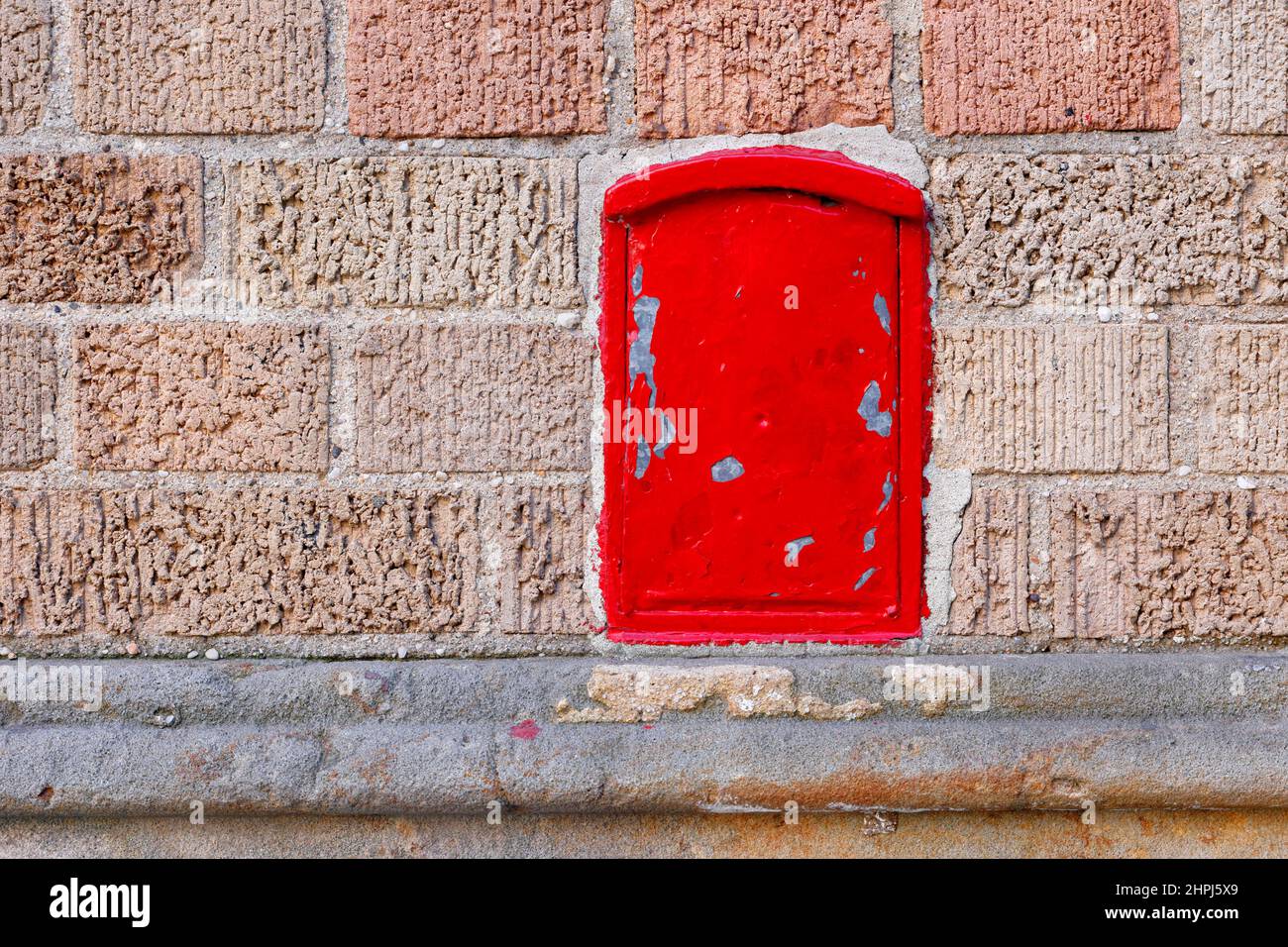 Eine kleine rot lackierte Metallbox, die in eine Ziegelwand eingebettet ist Stockfoto