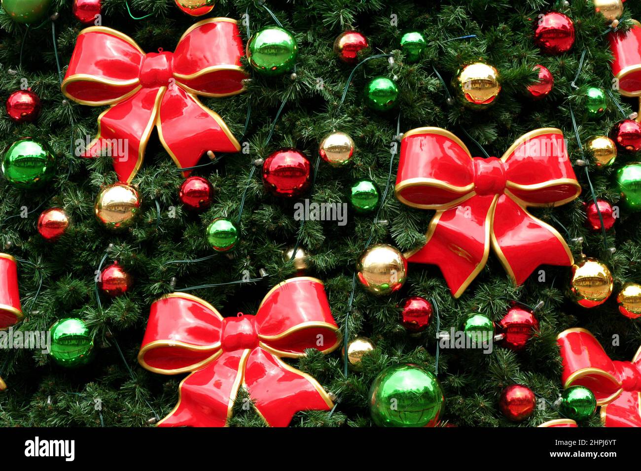 KERAMISCHE ROTE SCHLEIFEN MIT GOLD- UND GRÜNEN RÄNDERN, ROTE UND GOLDENE KUGELN SCHMÜCKEN EINEN WEIHNACHTSBaum IN ADELAIDE, SÜDAUSTRALIEN. Stockfoto