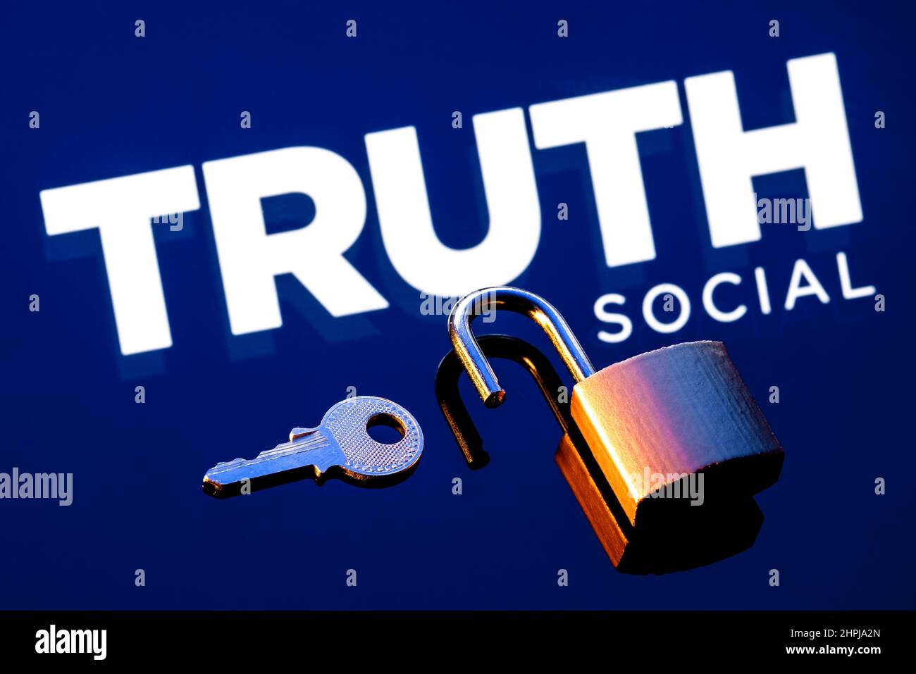 Ein offenes Sicherheitsschloss und Schlüssel auf dem Hintergrund des Logos des Truth Social-Netzwerks in Spiegelreflexion. Stockfoto