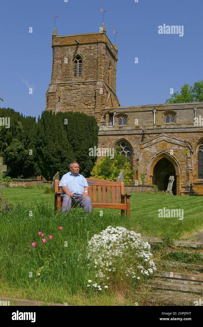 Außenansicht der Kirche St. Mary im Dorf Everdon, Northamptonshire, Großbritannien; älterer Mann auf einer Bank im Vordergrund Stockfoto