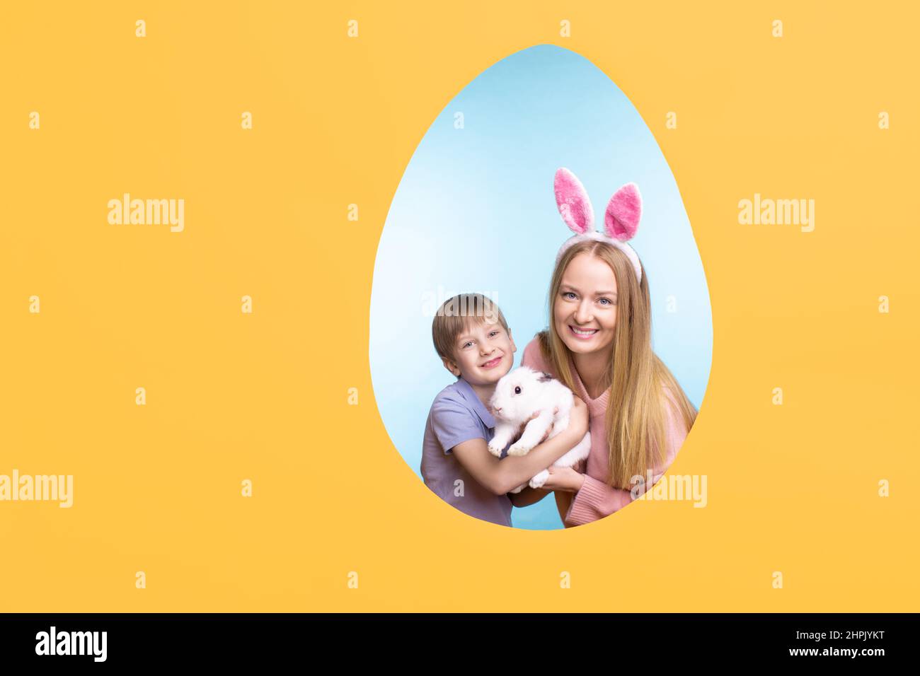 Ostern Grußkarte mit gelbem Copyspace und eiförmigen Rahmen mit niedlichen kleinen Jungen und seine Mutter hält weißen flauschigen niedlichen Kaninchen Stockfoto