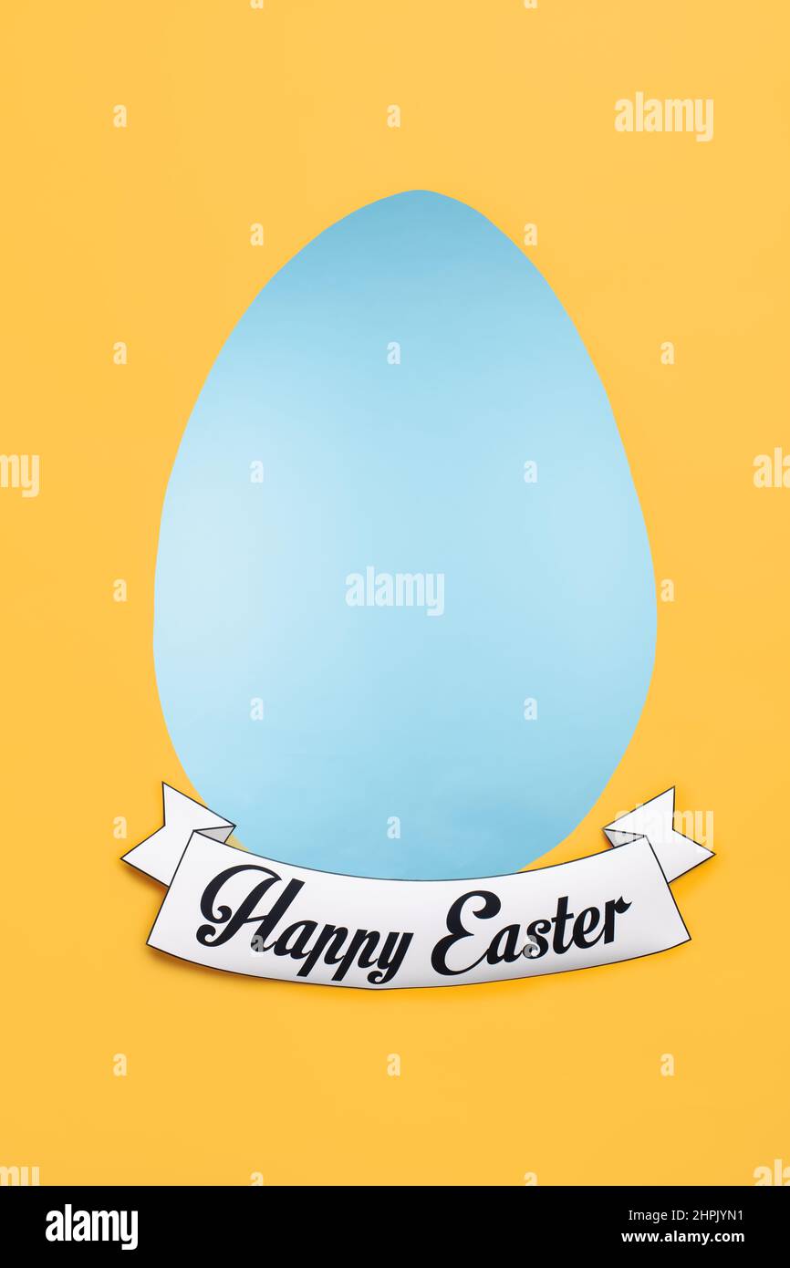 Vertikales Bild der Osterkarte mit der Form des hellblauen Eies und Grüßen des glücklichen Urlaubs unten und gelbem Copyspace herum Stockfoto