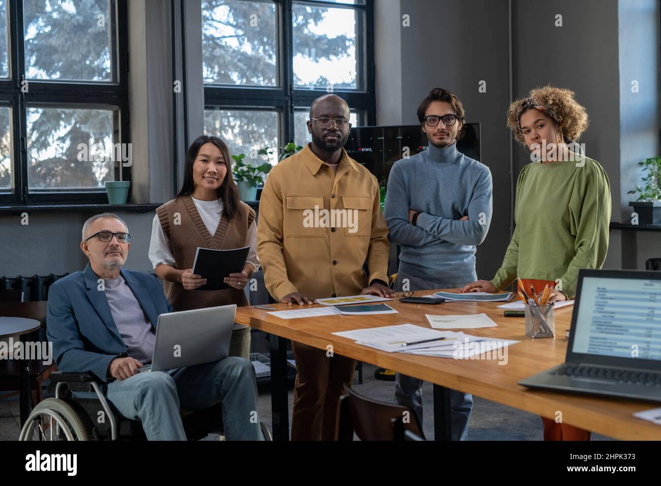 Große Gruppe von Kollegen aus verschiedenen Rassen in legerer Kleidung, die nach einer Schulung oder einem Seminar am Tisch im Sitzungssaal stehen Stockfoto