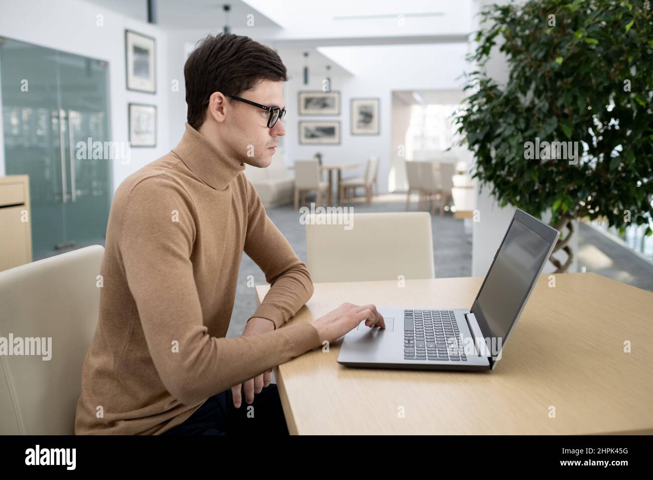 Junger ernsthafter Unternehmer in legerer Kleidung, der vor dem Laptop sitzt, während er über die Entwicklung der neuen Programmierung arbeitet Stockfoto