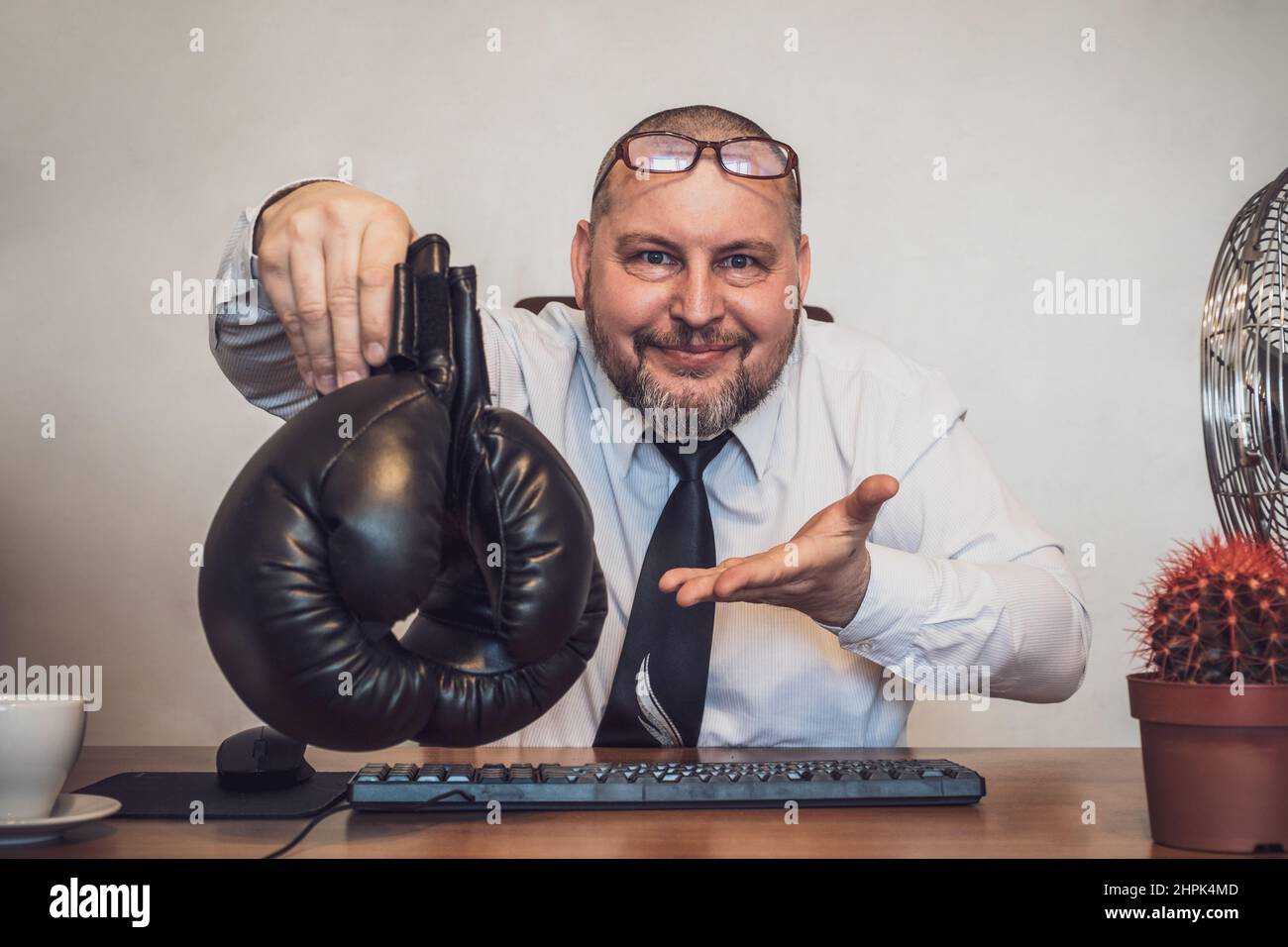 Ein lächelnder Geschäftsmann, der an einem Tisch sitzt, bietet höflich Boxhandschuhe an. Vorschläge zur Lösung geschäftlicher Probleme Stockfoto