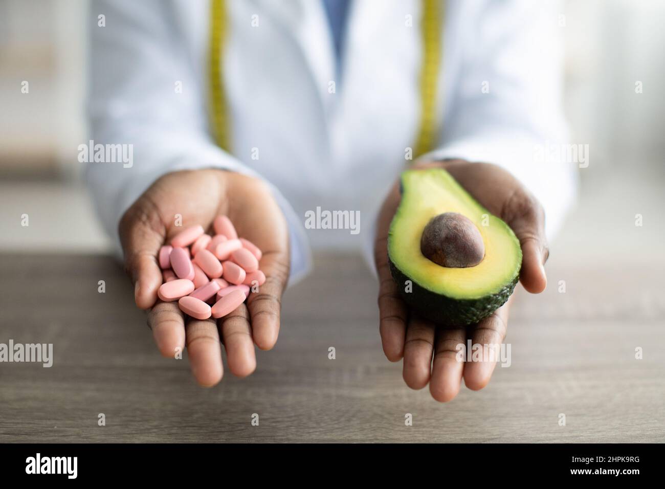 Gesundheits- und Diät-Konzept. Ernährungsberaterin hält Haufen von Pillen und die Hälfte von Avocado, arbeitet in der Klinik, Nahaufnahme Stockfoto