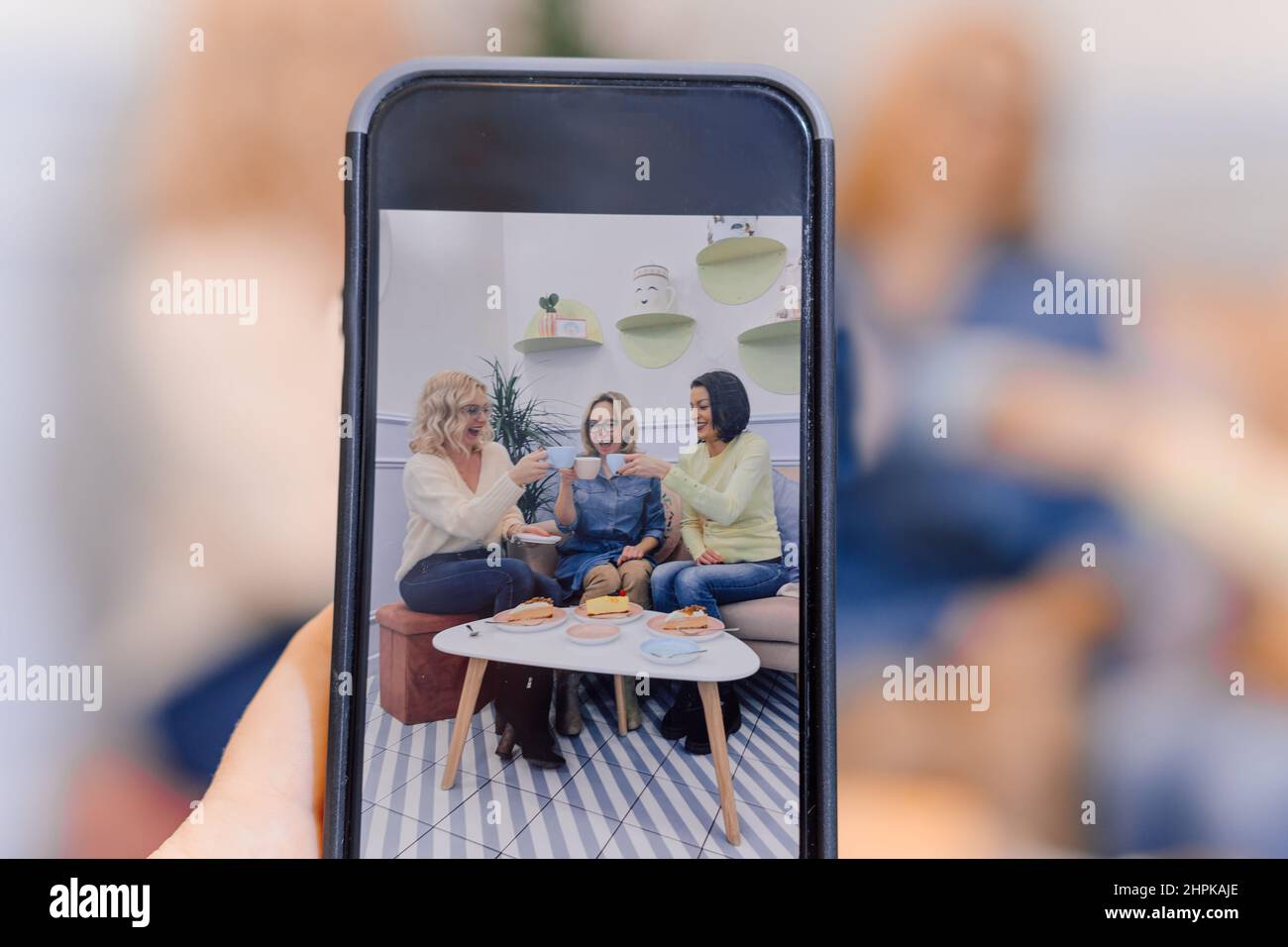 Weibliche Hände fotografieren auf dem Smartphone von drei Frauen, die gemeinsam Kuchen essen. Familie, die zusammen essen Stockfoto