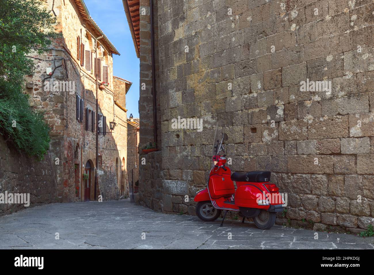 Das alte rote Moto lehnte sich an die Schattenmauer eines alten großen Backsteingebäudes in Monticchiello. Toskana, Italien Stockfoto