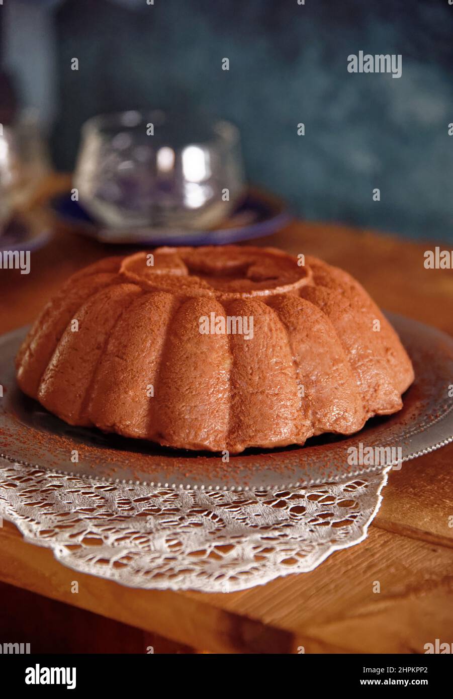 Chocolate handgemachter Pudding serviert in Silberplatte Teller und weiße Deckchen in Holztisch, im Feld zwei Gläser und blaue Tapete Stockfoto