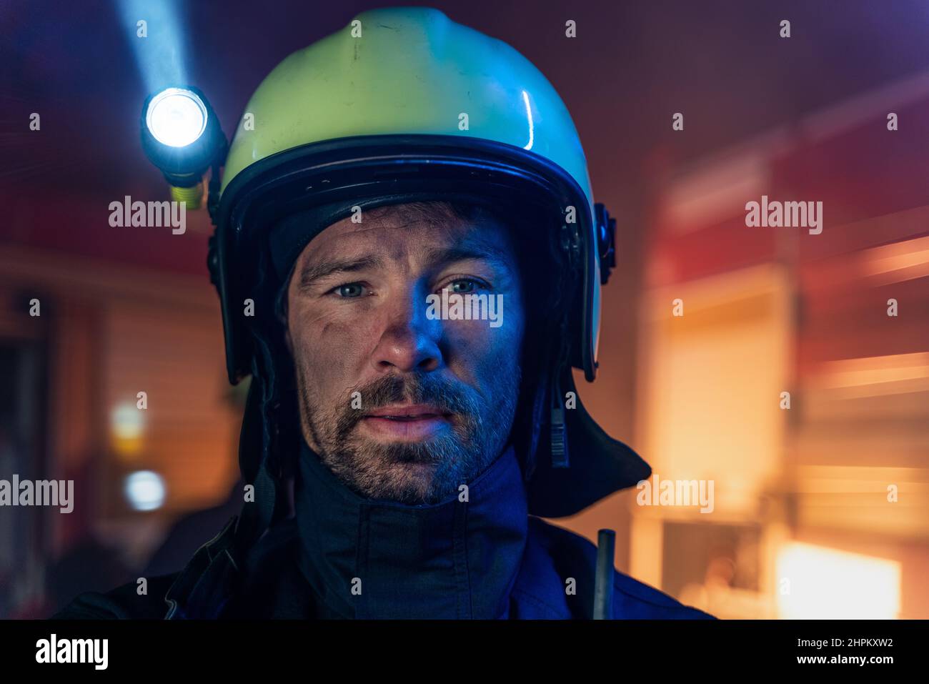 Porträt eines schmutzigen Feuerwehrmanns im Dienst mit Feuerwehrauto im Hintergrund in der Nacht, Blick auf die Kamera. Stockfoto