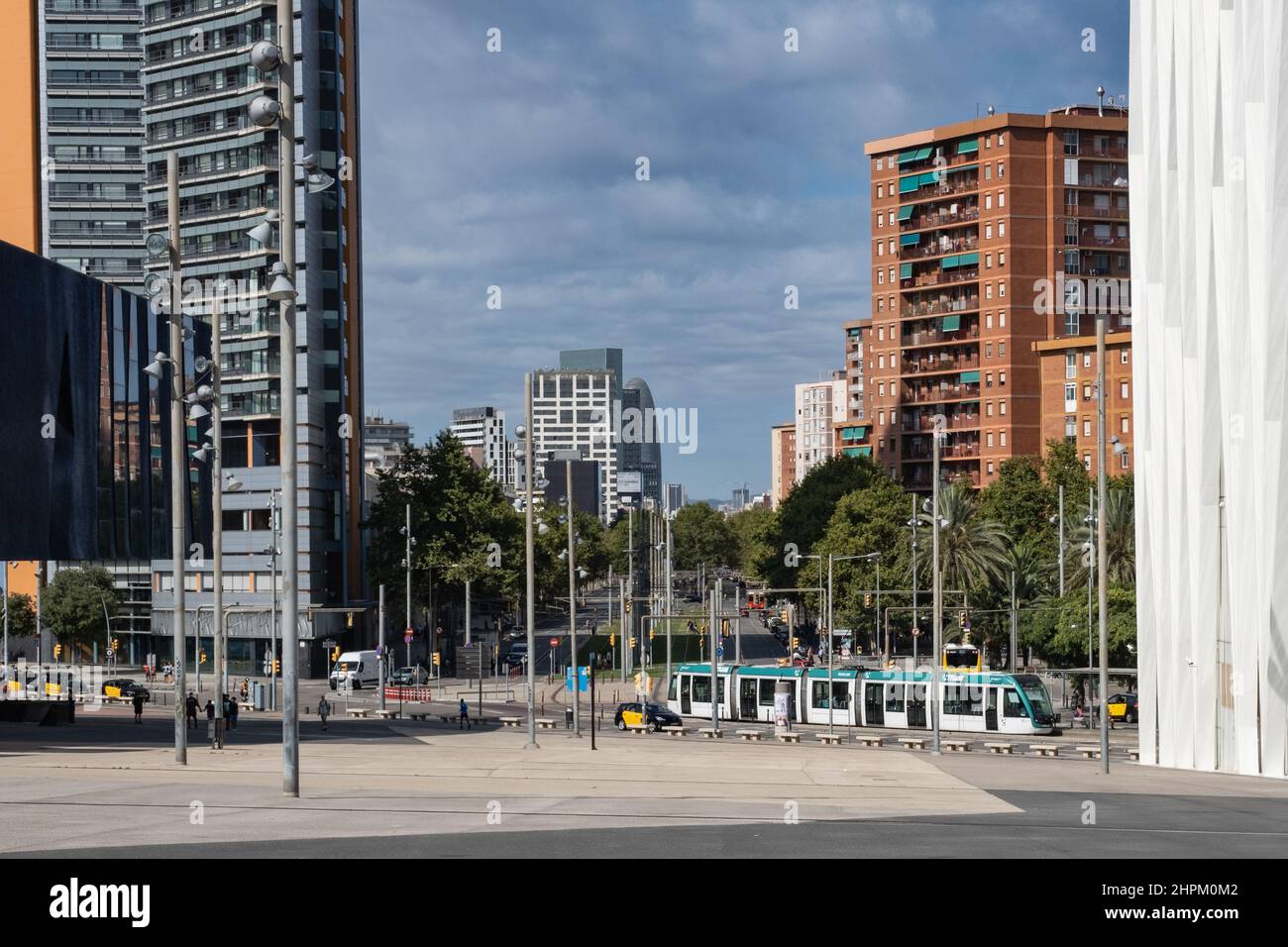 Blick auf die Av Diagonal in Barcelona, Spanien. Straßenbahn und Taxis fahren tagsüber entlang der Straße, Wolkenkratzer vor blauem Himmel im Hintergrund. Stockfoto