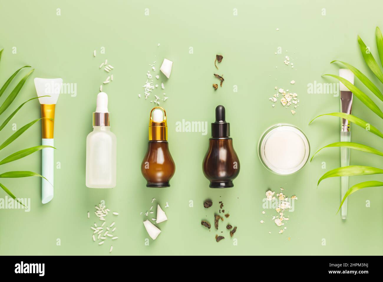 Fermentierte Schönheitspflege. Hande hat Reisserum, Grüntee-Serum, Haferflockencreme, Kokoswasser und kosmetisches Zubehör auf grünem Hintergrund hergestellt. Natürlich Stockfoto