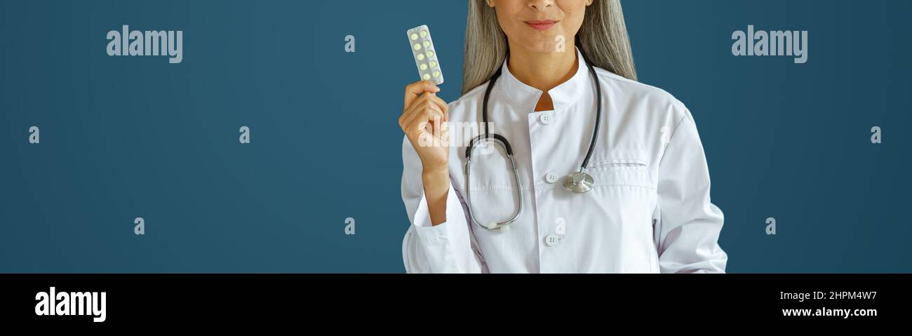 Positive reife Therapeutin zeigt Pillen Blister stehen auf blauem Hintergrund Stockfoto