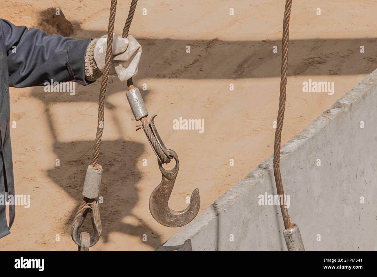 Die Hand des Bauarbeiters männlich nimmt einen schweren Eisenhaken-Hebemechanismus mit einem Stahlseil auf eine Beton-, Zementstruktur. Stockfoto