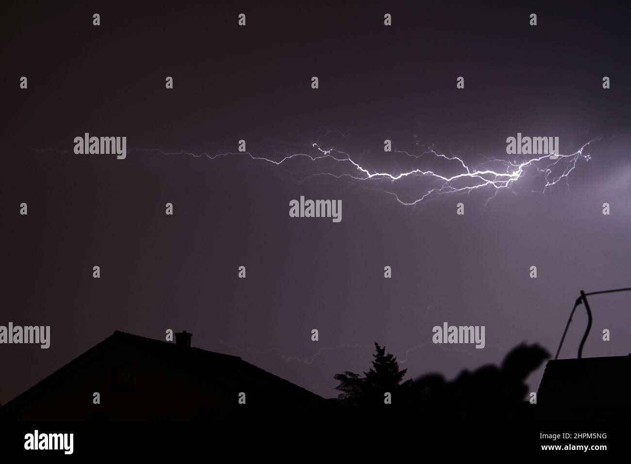 Blitze blitzen über einen stürmischen Nachthimmel mit Häusern Stockfoto