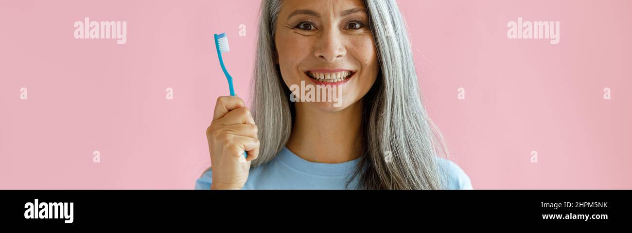 Eine fröhliche asiatische Frau mittleren Alters hält die Zahnbürste auf rosa Hintergrund Stockfoto