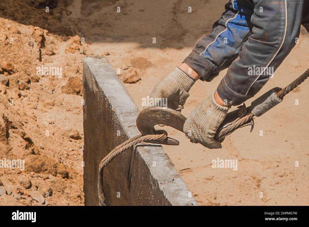 Die Hand des Bauarbeiters männlich nimmt einen schweren Eisenhaken-Hebemechanismus mit einem Stahlseil auf eine Beton-, Zementstruktur auf die Konstruktion Stockfoto