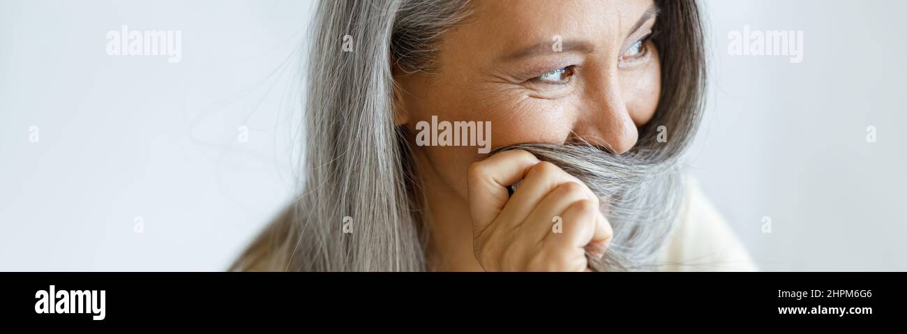 Asiatische Frau mittleren Alters versteckt Gesicht mit grauen Haaren sitzen auf hellem Hintergrund Stockfoto