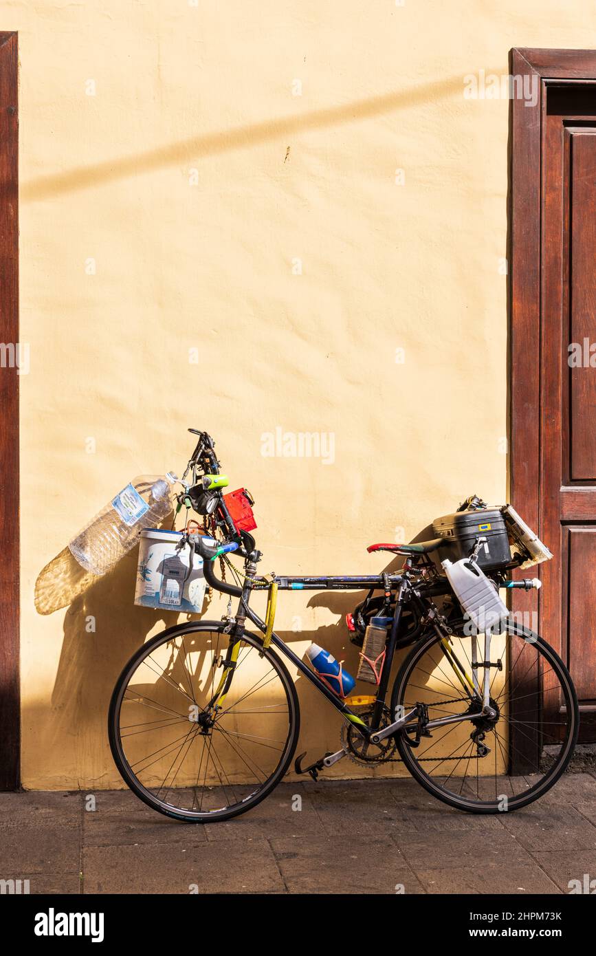 Fahrrad mit vielen Kunststoffbehältern, die an einer Wand in der Sonne in San Cristobal de La Laguna, Teneriffa, Kanarische Inseln, Spanien, geparkt sind Stockfoto
