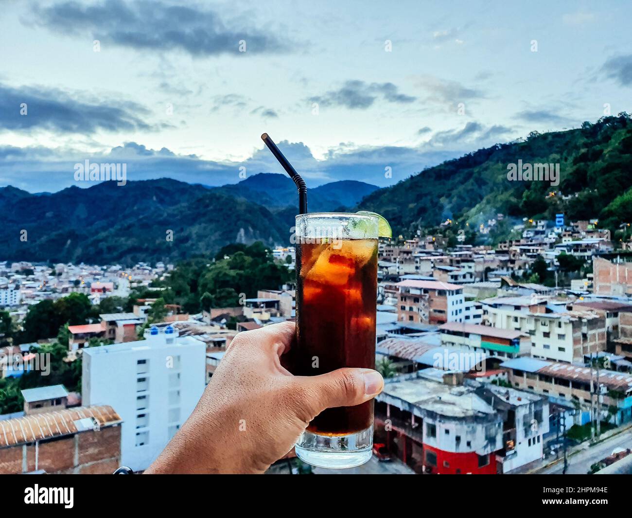 Hand eines Mannes mit einem Getränk mit Blick auf die Stadt Chanchamayo im Departement Junin in Peru Stockfoto