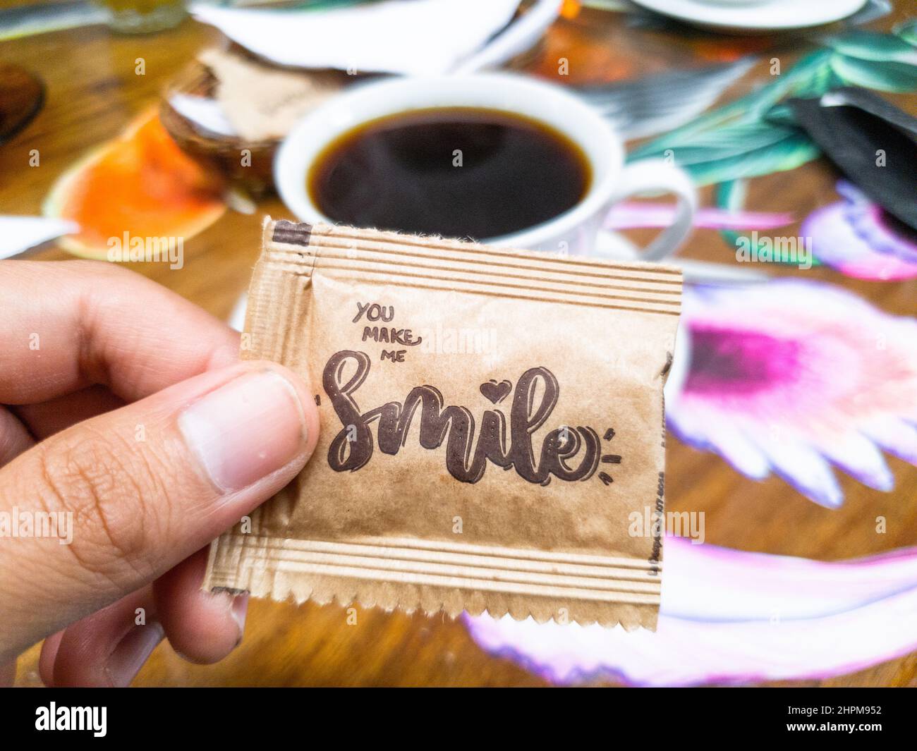 Zuckerumschlag, wo es sagt Lächeln mit einer Tasse Kaffee im Hintergrund Stockfoto