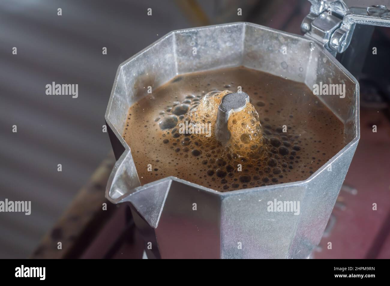 Italienische Kaffeemaschine, die Kaffee mit Rauch und Tröpfchen zubereitet, die mit natürlichem Licht ausstrahlen, Frühstückskonzept. Stockfoto