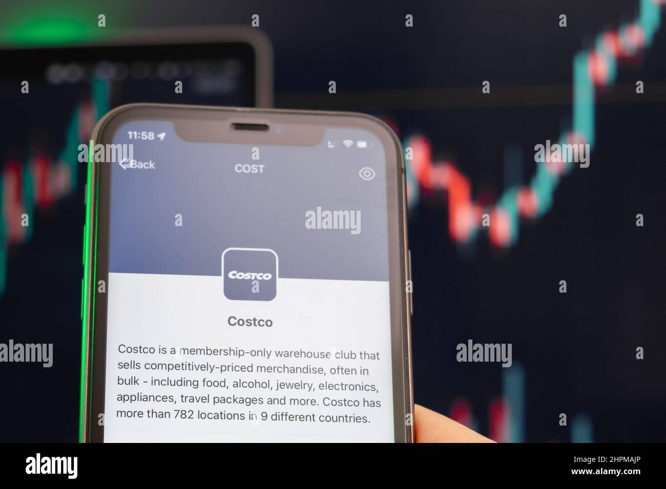 Der Aufwärtstrend der Aktienkursen von Costco mit Grafiken im Hintergrund. Man hands Holding a Smartphone with Logo on the screen, February 2022, San Francisco, USA. Stockfoto