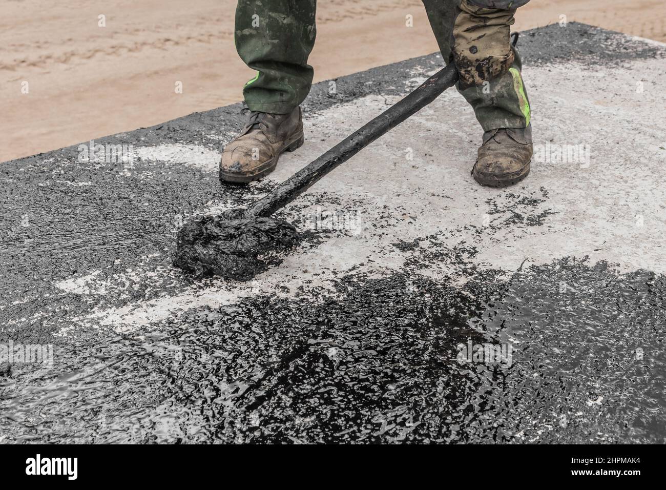 Ein Bauarbeiter ist mit schmutzigen manuellen Arbeiten beschäftigt, um die Betonoberfläche der Struktur zu reparieren und schwarzen Bitumen-Abdichtungsteer aufzutragen. Stockfoto