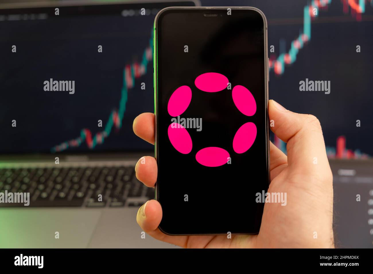Polkadot DOT Kryptowährung Logo auf dem Bildschirm eines Smartphones in mans Hand mit einem wachsenden Trend auf dem Chart auf grünem Hintergrund. Stockfoto