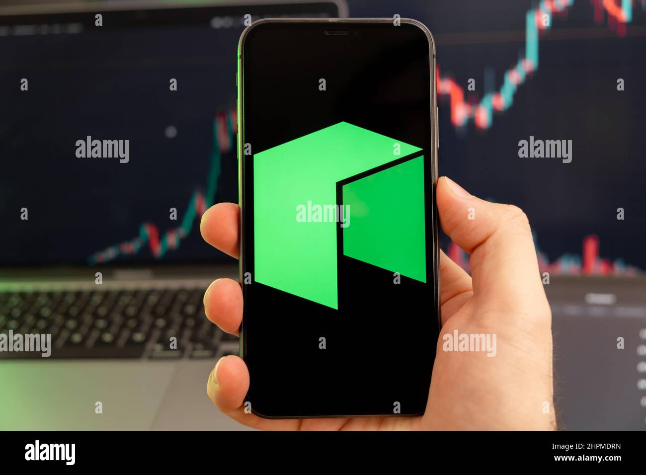 Neo Kryptowährung Logo auf dem Bildschirm eines Smartphones in mans Hand mit einem wachsenden Trend auf dem Chart auf einem grünen Hintergrund. Stockfoto