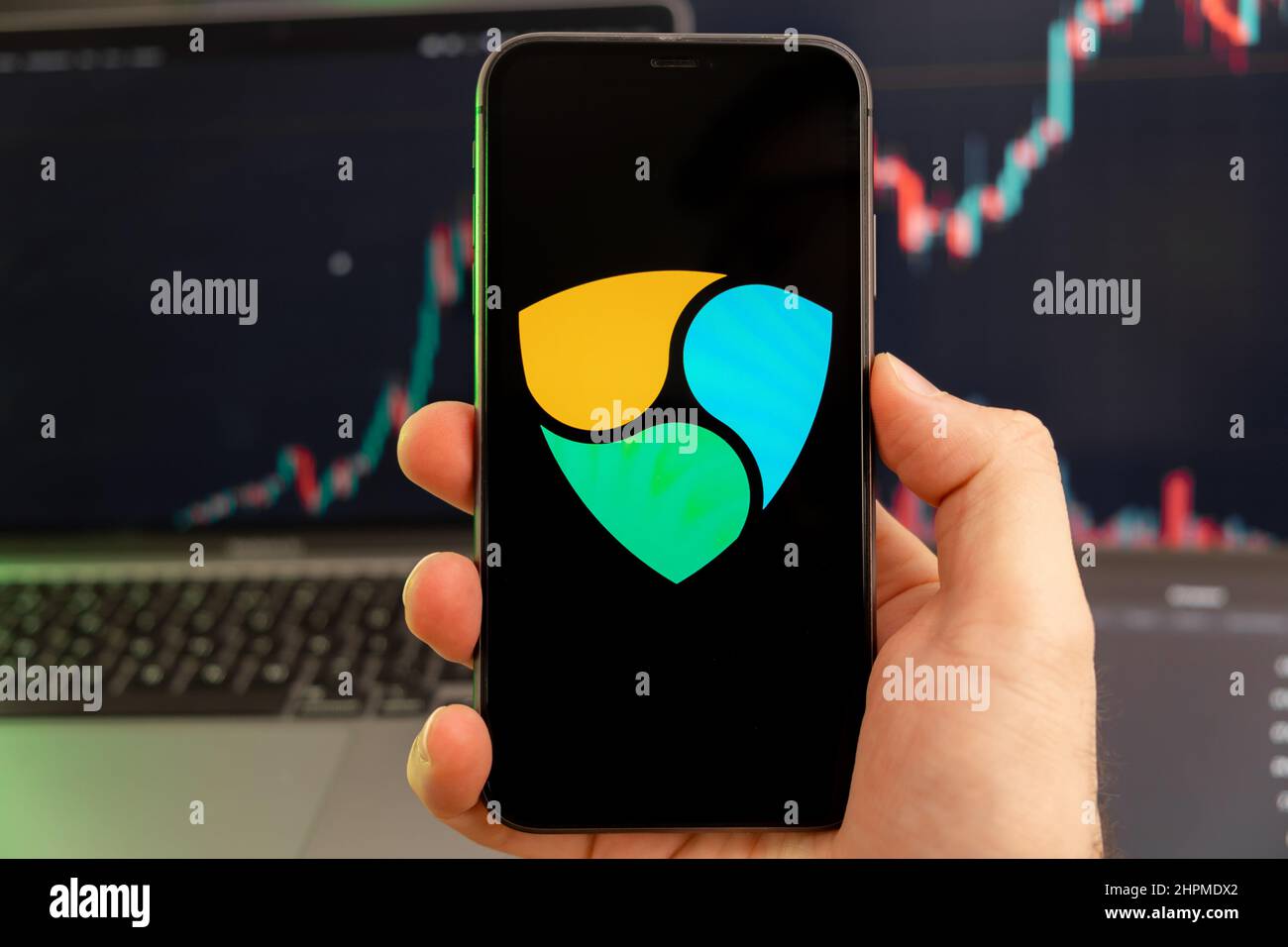 NEM XEM Kryptowährung Logo auf dem Bildschirm eines Smartphones in Mans Hand mit einem wachsenden Trend auf dem Chart auf grünem Hintergrund. Stockfoto