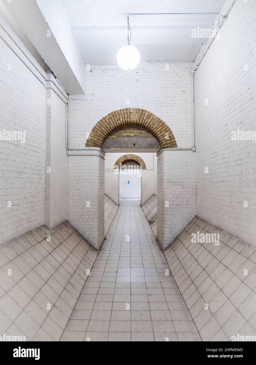 Weißer Durchgang. Ein abstrakter Blick auf die Symmetrie der alten viktorianischen Londoner Industriearchitektur und einen weiß getünchten Tunnelpfad. Stockfoto