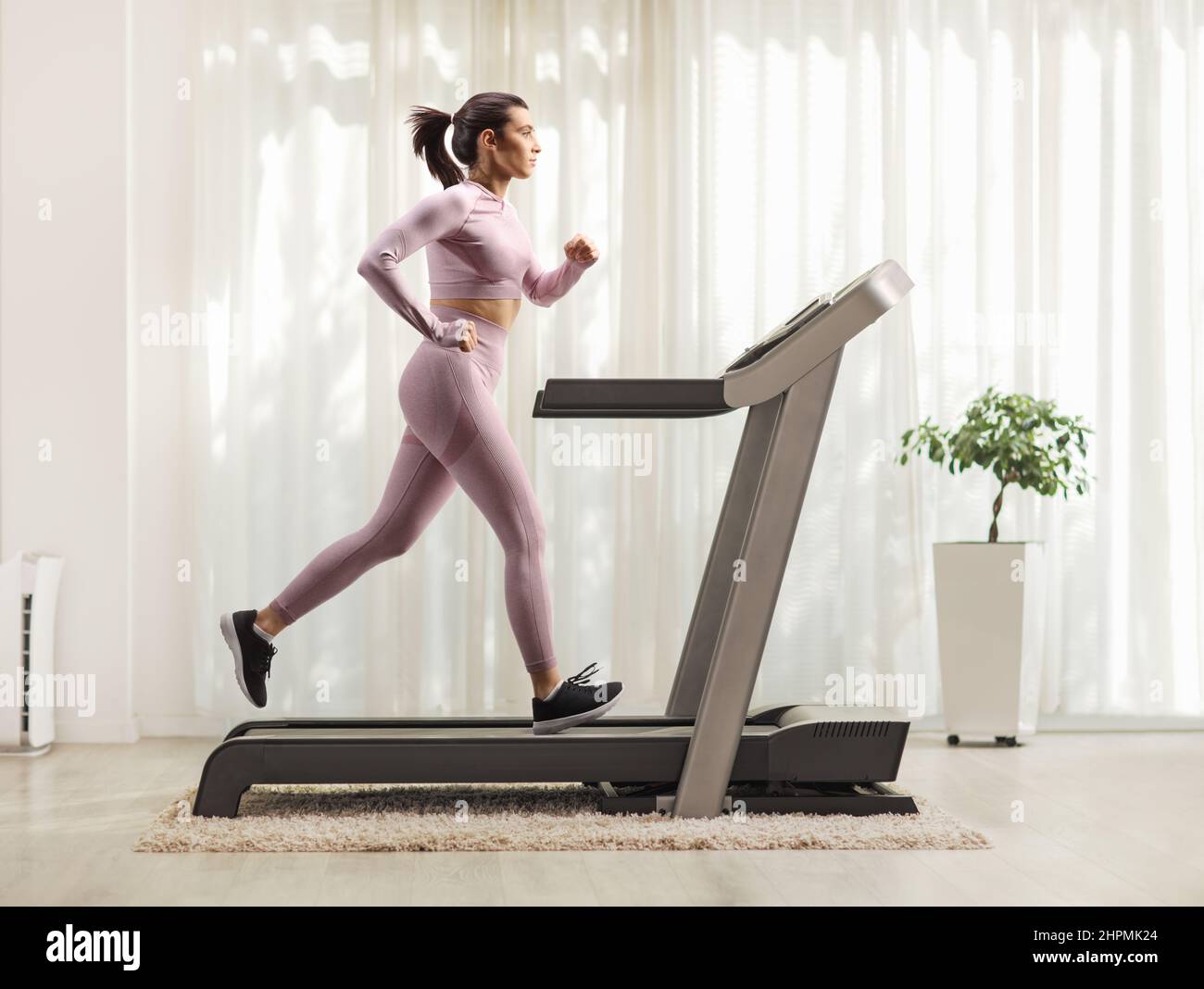 Aufnahme einer Frau im Crop-Top und Leggings, die zu Hause auf einem Laufband läuft Stockfoto