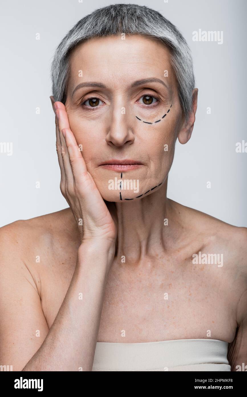 Reife Frau mit Falten und markierten Linien Blick auf Kamera isoliert auf grau Stockfoto