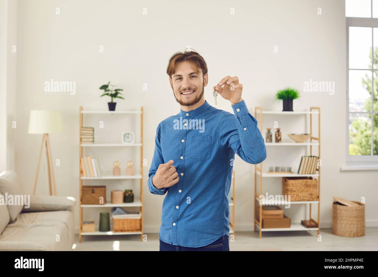 Der Mann, der erster Käufer, Hausbesitzer oder Mieter der Wohnung ist, zeigt die Schlüssel, während er die Kamera anschaut. Stockfoto