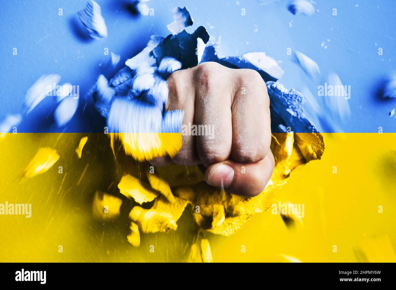 Eine Faust stanzt durch eine Betonwand mit den Farben der ukrainischen Nationalflagge. Das Konzept der russischen Aggression gegen die Ukraine Stockfoto