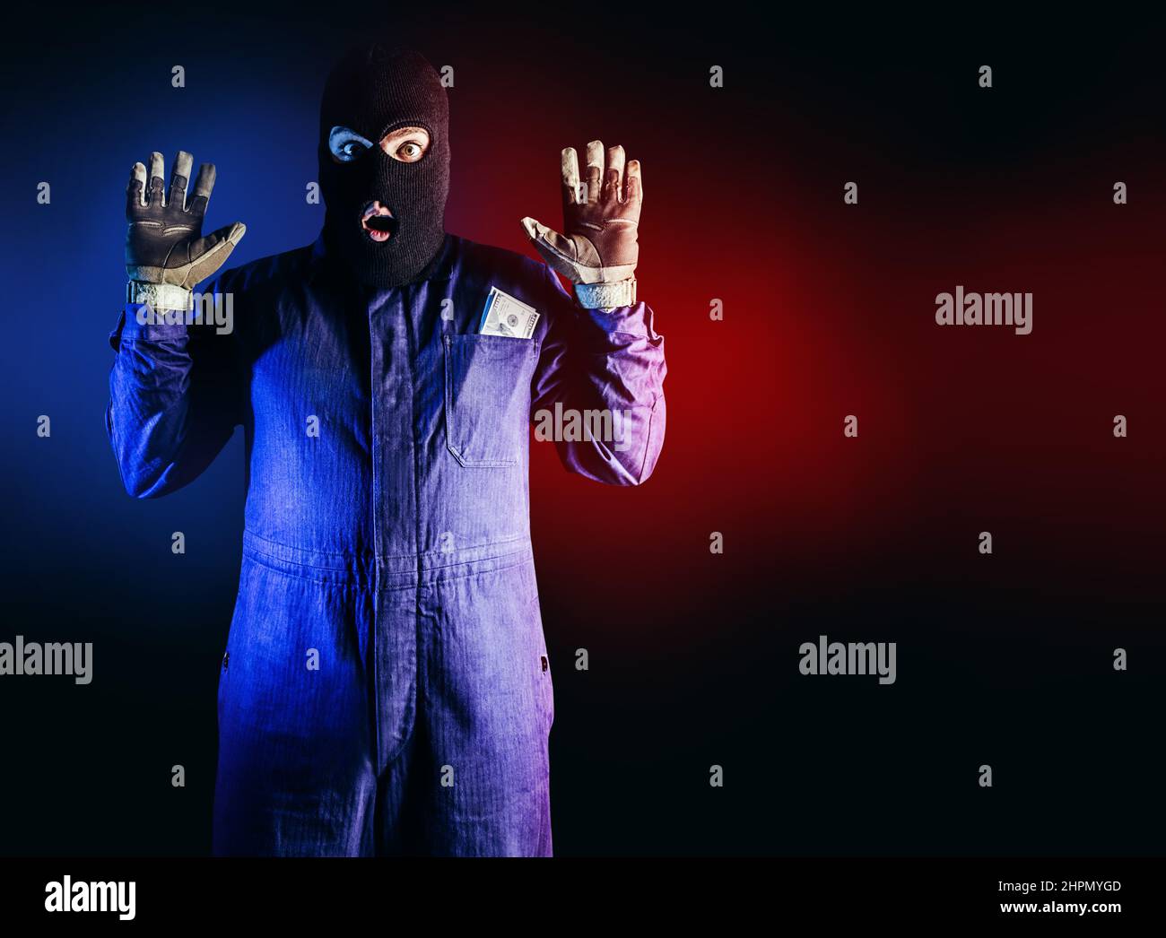 Foto von gefangenem Räuber in Maske, Overalls, Handschuhen und Geldbeutel, die auf rotem und blauem Hintergrund stehen. Stockfoto