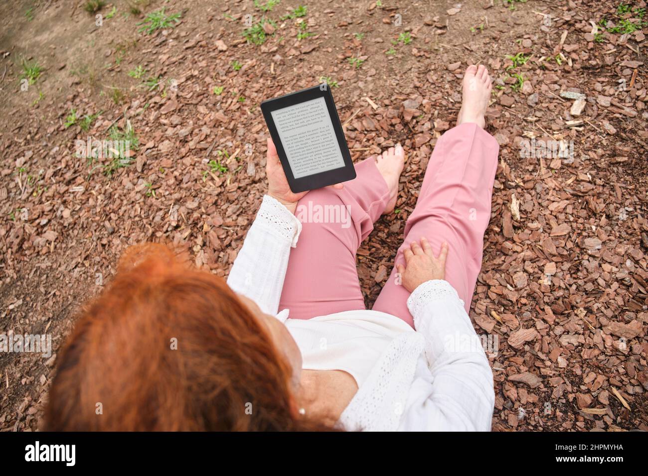 Unerkennbare reife Frau, die ein eBook auf einem elektronischen Leser liest, der in einem Park sitzt. Konzepte: Technologie und Lesen. Stockfoto