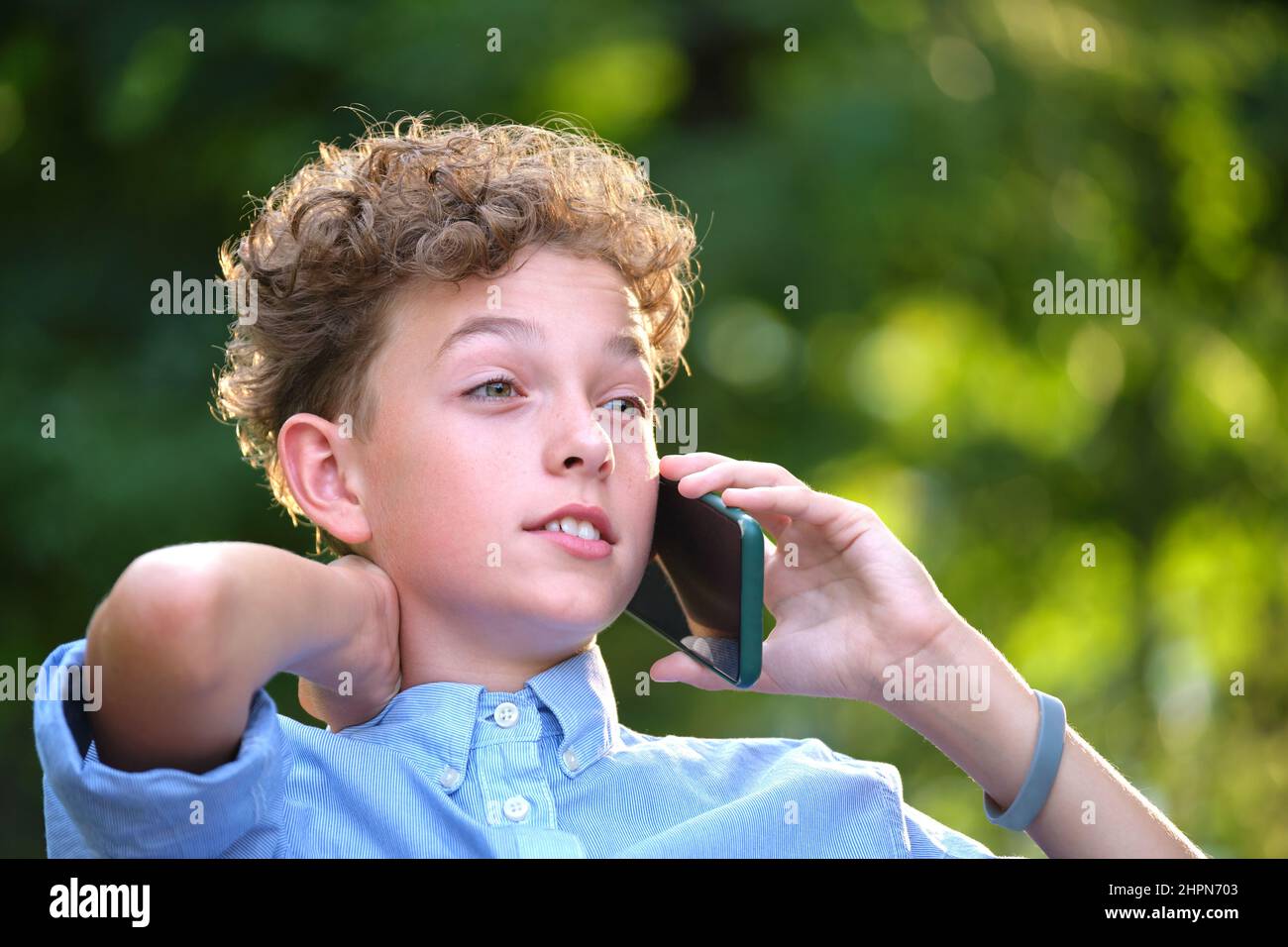 Junger, rätselhafter Junge, der im Sommerpark mit dem Handy telefoniert. Stockfoto