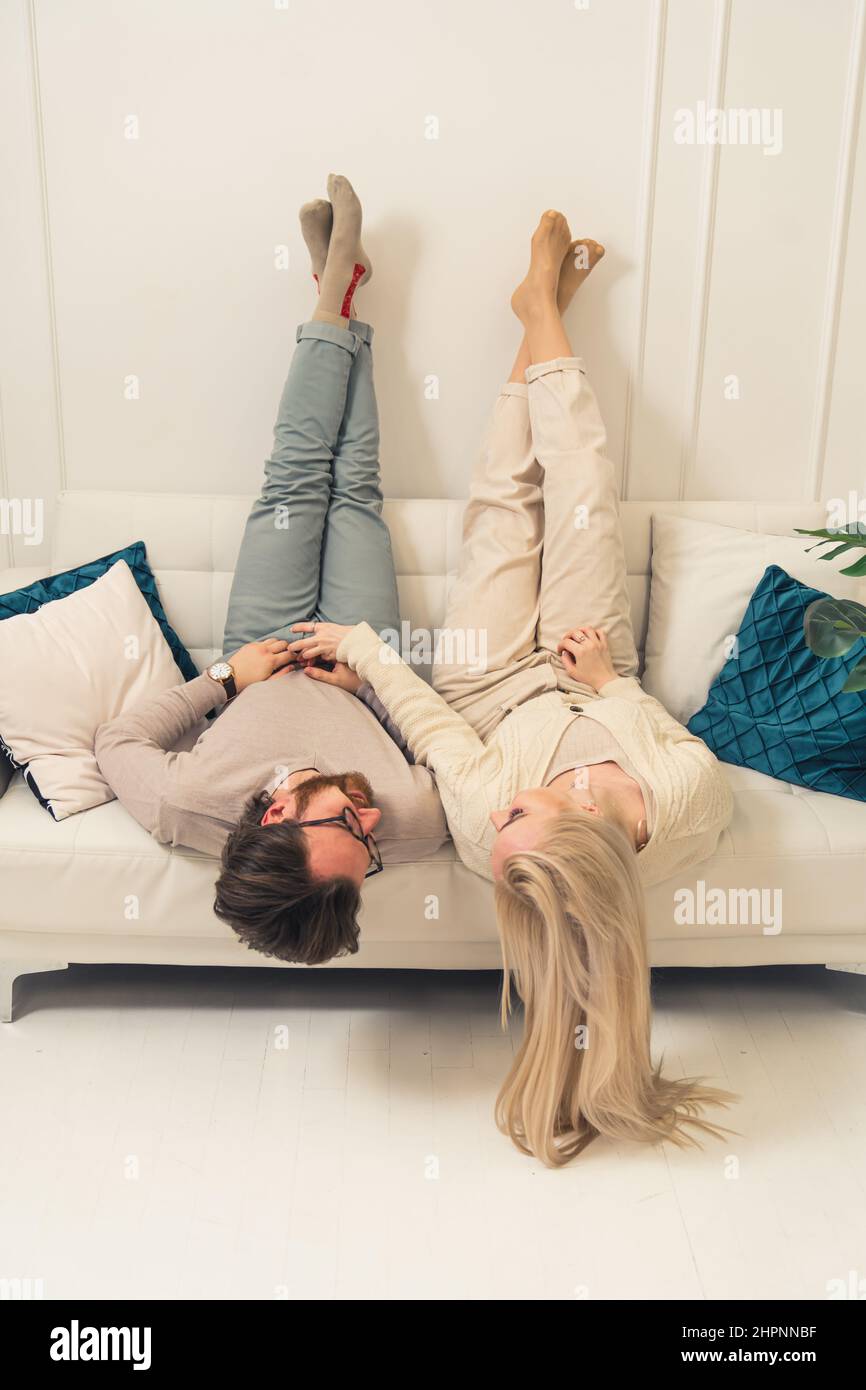Vertikale Foto kaukasische blonde langhaarige Frau und ihr brünstiger Ehemann auf einer Couch mit ihren Beinen nach oben liegen. Hochwertige Fotos Stockfoto