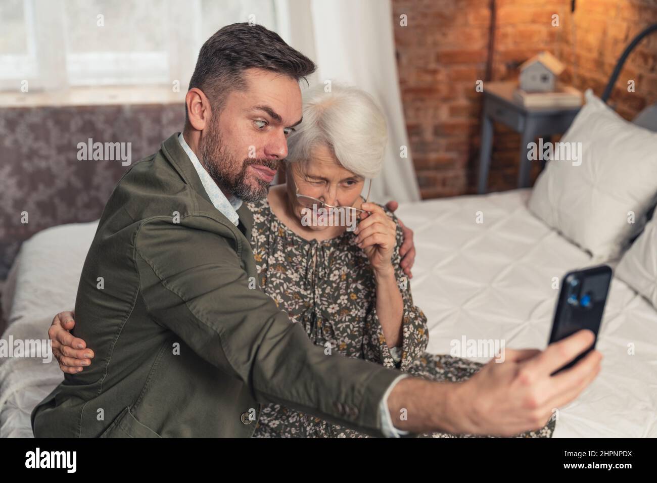 Ältere Großmutter und ihr ältester Enkel machen dumme Gesichter und machen ein Selfie mit schwarzem Smartphone. Hochwertige Fotos Stockfoto