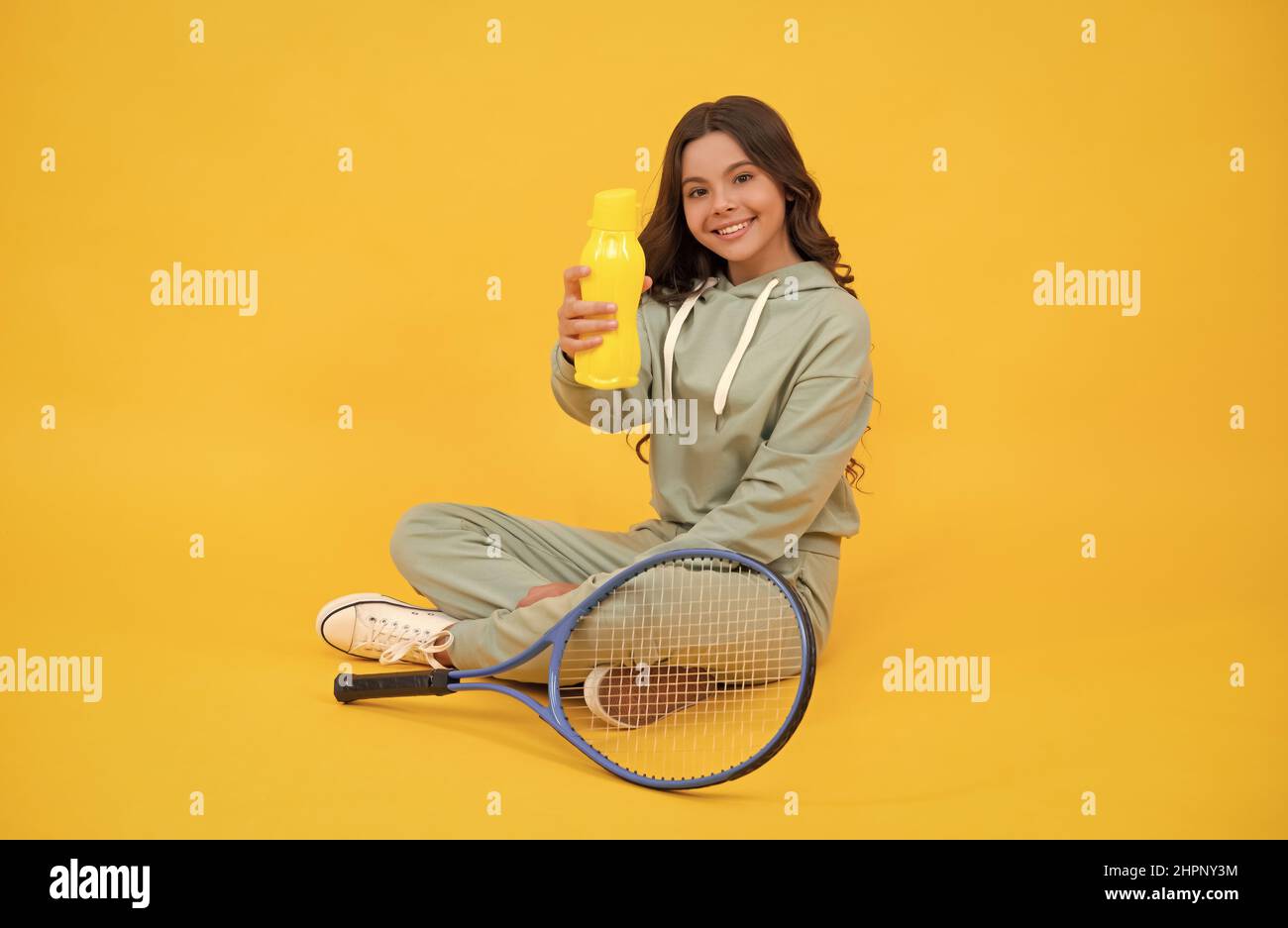 Kind sitzen mit Schläger und Wasserflasche. Kind mit Tennisschläger. Teen Mädchen trinken Wasser Stockfoto