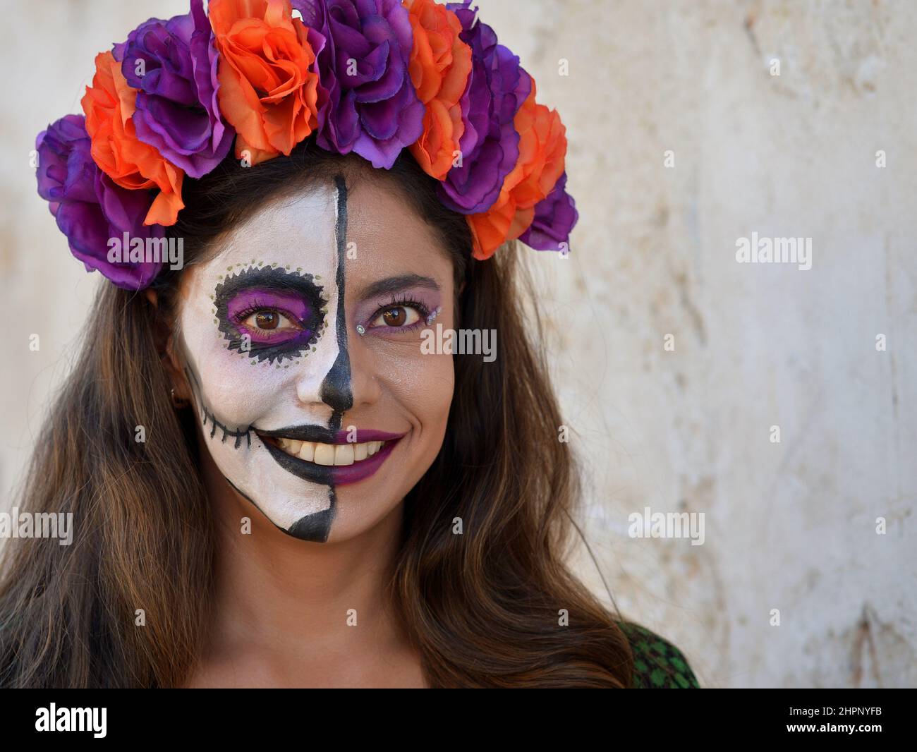 Junge schöne kaukasische Frau mit gruseliger weißer traditioneller Halbgesichtsbemalung am mexikanischen Tag der Toten (Día de los Muertos) lächelt den Betrachter an. Stockfoto