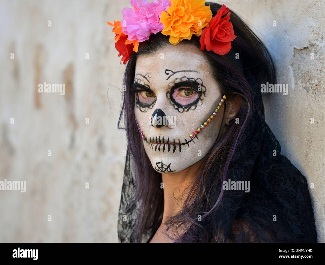 Junge schaurige kaukasische Frau mit gruseligen weißen Gesichtsbemalungen und bunten Blumen am mexikanischen Tag der Toten (Día de los Muertos) schaut den Betrachter an. Stockfoto