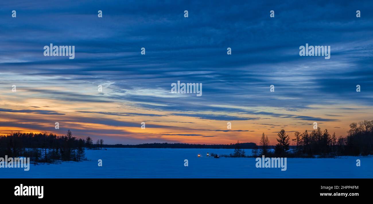 Schneemobilfahrer während der blauen Stunde auf der Chippewa-Flowage im Norden von Wisconsin. Stockfoto