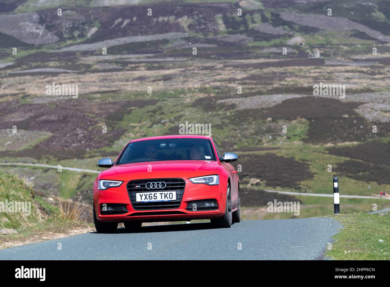 Rotes Audi-Auto, das auf einer einspurigen Straße über Moorland im Yorkshire Dales National Park, Großbritannien, fährt. Stockfoto