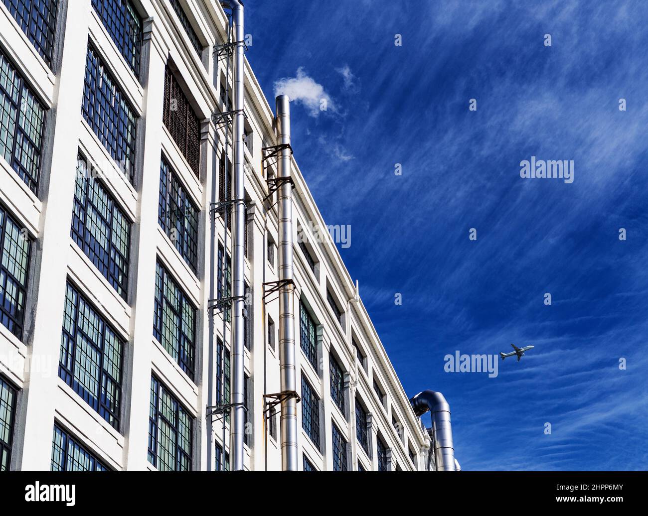 Blick in den niedrigen Winkel des mehrstöckigen Industriegebäudes mit dramatischem blauen Himmel und einem kleinen Luftmatratenbild. Stockfoto